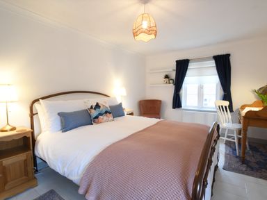 A bedroom with a double bed, bedside tables with lamps, a chair, a window with curtains, and a wooden desk with a chair at Rosedene Rickinghall