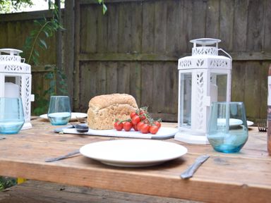 An outdoor wooden table set with plates forks blue glasses white lanterns bread and tomatoes at Rosedene Rickinghall