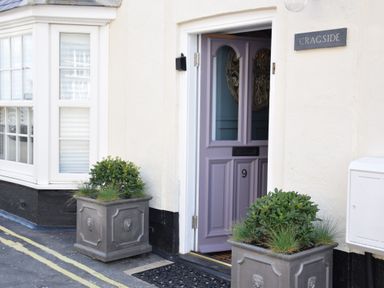 A partially open purple door numbered 9 with two gray planters containing green plants outside and a sign that reads cragside in Aldeburgh