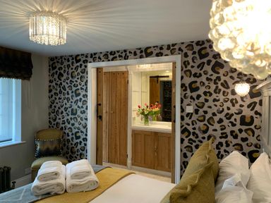 A bedroom with leopard print wallpaper a bed with towels green cushions and a chair at Cragside Aldeburgh