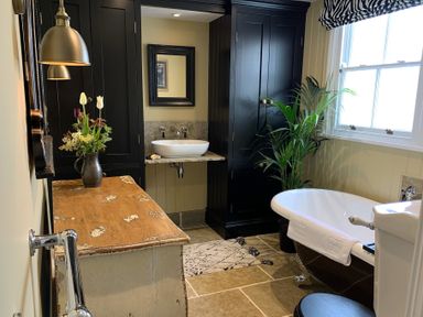 A bathroom with a freestanding bathtub a wooden cabinet a vessel sink and a potted plant at Cragside Aldeburgh