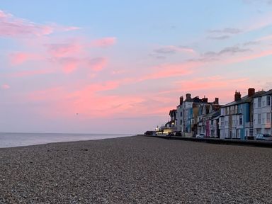 A pebble beach with a row of houses along the shore and a pink and blue sky at Cragside Aldeburgh