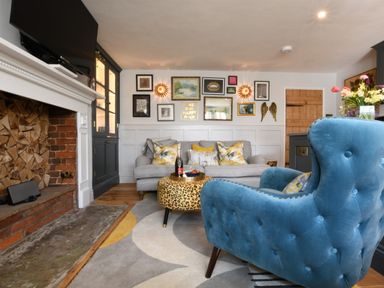 A living room with a blue armchair a grey sofa and a leopard print ottoman at Cragside Aldeburgh