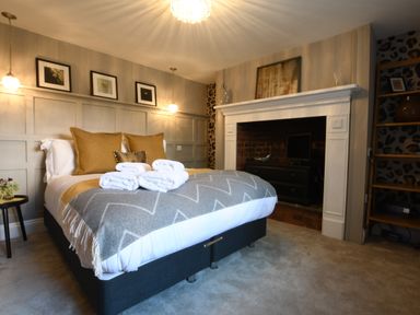 A bedroom with a bed with towels on it a fireplace and framed pictures on the wall at Cragside Aldeburgh