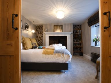 A bedroom with a bed with towels and pillows next to a fireplace with shelves and a window with flowers at Cragside Aldeburgh