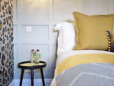 A bedroom corner with a bed and side table with a small vase of flowers at Cragside Aldeburgh in Aldeburgh