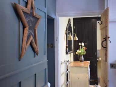 A hallway with a star-shaped wooden sign on a blue wall and a small table with flowers near a black cabinet at Cragside Aldeburgh