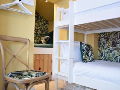 A bedroom with a white bunk bed a wooden chair and a small seating nook with patterned cushions at Cragside Aldeburgh in Aldeburgh