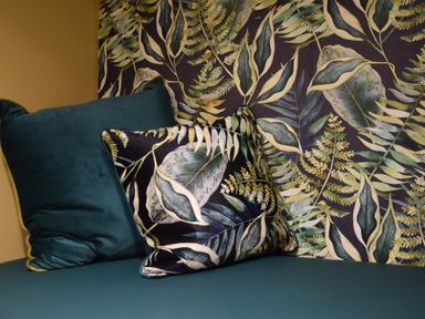 Two pillows on a blue couch with leaf patterned wallpaper at Cragside Aldeburgh
