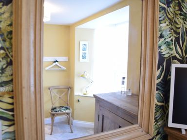A wooden chair with patterned cushion near a small wooden cabinet and a yellow desk lamp in front of a window at Cragside Aldeburgh
