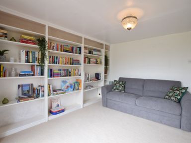 A room with white bookshelves filled with books and a gray sofa with two patterned cushions at Skelder Parham in Parham Near Framlingham