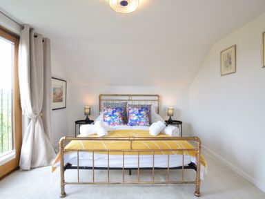 A bedroom with a metal bed frame yellow blanket and two floral pillows at Skelder Parham in Parham Near Framlingham