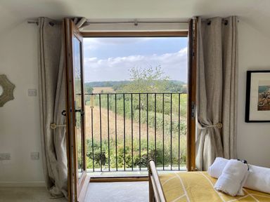 A bedroom with an open double door leading to a balcony overlooking fields at Skelder Parham in Parham Near Framlingham