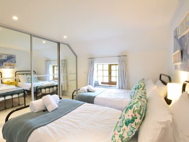 A bedroom with two single beds a window with curtains and mirrored wardrobes at Skelder Parham in Parham Near Framlingham