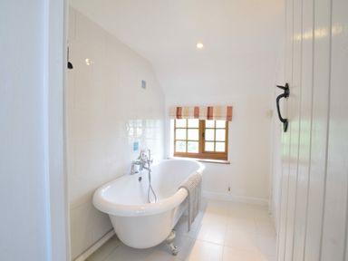 A bathroom with a white clawfoot bathtub a striped window blind and white tiled walls at Skelder Parham in Parham Near Framlingham