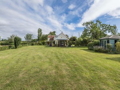 A large lawn with a house in the center and a wooden shed on the right at Skelder Parham in Parham Near Framlingham