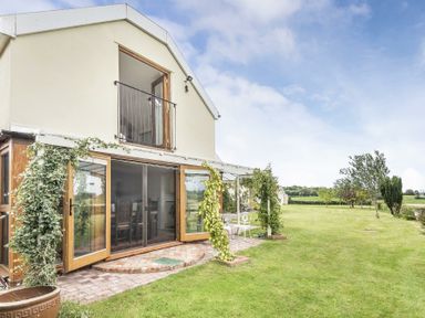 A house with open wooden doors and a balcony overlooking a lawn with trees at Skelder Parham in Parham Near Framlingham