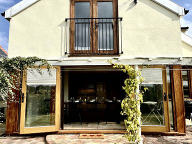 A house exterior with wooden framed glass doors and a balcony with a black metal railing at Skelder Parham in Parham Near Framlingham