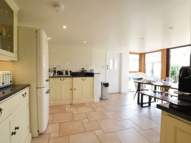 A kitchen with cream cabinets a black countertop a white fridge a toaster a dining table with chairs and a bench at Skelder Parham in Parham Near Framlingham