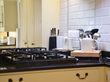 A kitchen countertop with a gas stove, a white teapot on a wooden tray, a knife block, paper towel roll, and kitchen utensils at Skelder Parham in Parham Near Framlingham