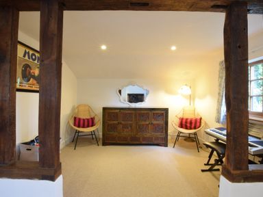 A room with two wicker chairs with cushions a decorative cabinet a mirror a floor lamp and a keyboard at Skelder Parham Parham Near Framlingham