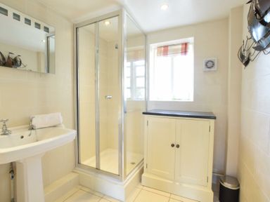 A bathroom with a pedestal sink a glass shower enclosure a cabinet under a window and a trash bin at Skelder Parham Parham Near Framlingham