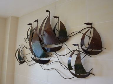 A metal wall sculpture of multiple sailboats mounted on a light tiled wall at Skelder Parham in Parham Near Framlingham