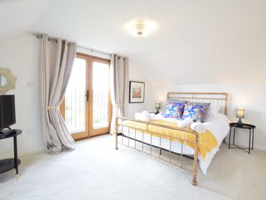 A bedroom with a metal bed frame blue floral pillows and yellow blanket near glass doors with curtains at Skelder Parham in Parham Near Framlingham