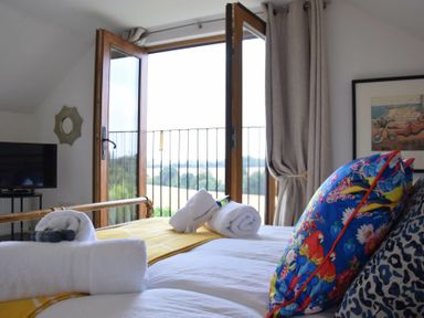A bedroom with a bed with colorful cushions and rolled towels near an open balcony door at Skelder Parham in Parham Near Framlingham