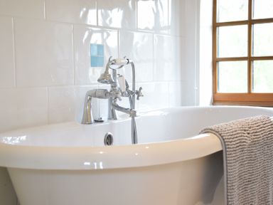 A white bathtub with chrome faucet and showerhead and gray towel hanging over the edge near a window at Skelder Parham in Parham Near Framlingham
