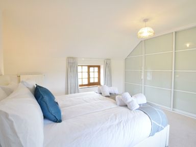 A bedroom with a bed with white and blue pillows towels on bed and sliding wardrobe doors at Skelder Parham in Parham Near Framlingham