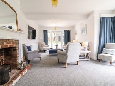 A living room with armchairs a blue ottoman and a brick fireplace at High Ground Reydon in Reydon