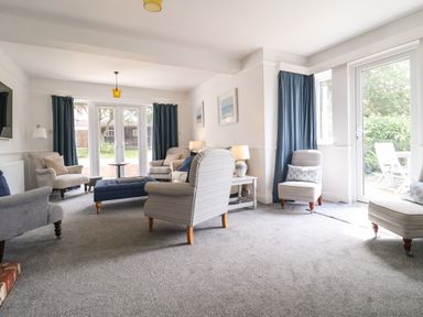 A living room with armchairs a blue ottoman and large windows at High Ground Reydon in Reydon