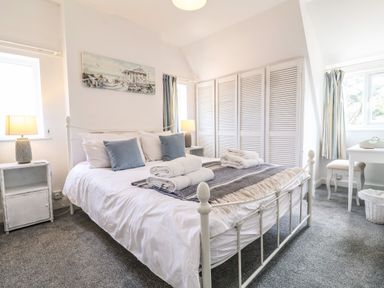 A bedroom with a white metal bed frame towels on the bed bedside tables with lamps a desk and chair and built-in wardrobes at High Ground Reydon in Reydon