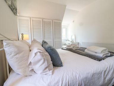 A bedroom with a bed with pillows and folded towels a vanity table and white louvered closet doors at High Ground Reydon