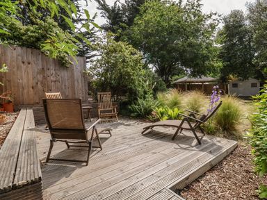 An outdoor wooden deck with chairs surrounded by plants, trees, and a wooden fence at High Ground, Reydon