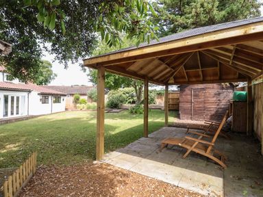 A backyard with a wooden gazebo and two chairs on a paved area at High Ground Reydon in Reydon