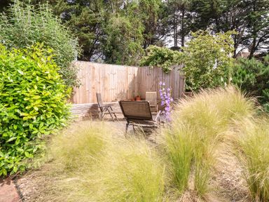 An outdoor seating area with wooden chairs and a wooden fence surrounded by plants and trees at High Ground Reydon in Reydon