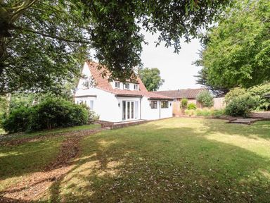 A white house with a tiled roof surrounded by green trees and a grassy lawn at High Ground Reydon