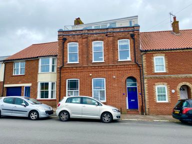 A street view of a brick building with blue doors and several parked cars at Pier View Southwold