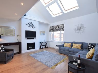 A living room with skylights a gray sofa with yellow cushions and a wall-mounted television at Pier View Southwold