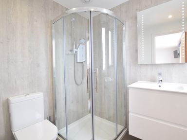 A bathroom with a shower with glass doors a toilet and a sink with a mirror at Pier View Southwold in Southwold