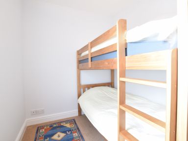 A small bedroom with wooden bunk beds and a colorful rug on the floor at Pier View Southwold