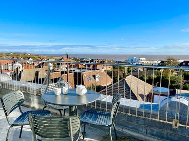 A balcony with a round table and four chairs overlooking rooftops and the sea at Pier View Southwold