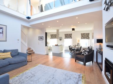 An open plan living room with a blue sofa a black armchair a dining table and a kitchen area at Pier View Southwold