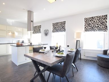A dining area with a table set for four and a kitchen with white cabinets and an island at Pier View Southwold
