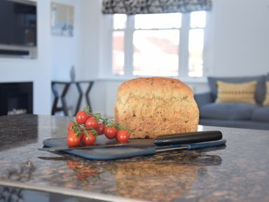 A kitchen island with a loaf of bread cherry tomatoes and a knife in a living room at Pier View Southwold