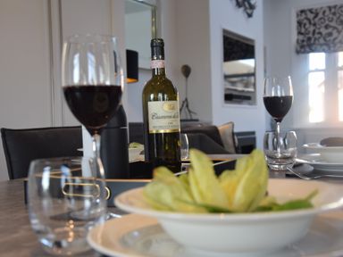 A dining table set with wine glasses a bottle of red wine a bowl of salad and plates at Pier View Southwold
