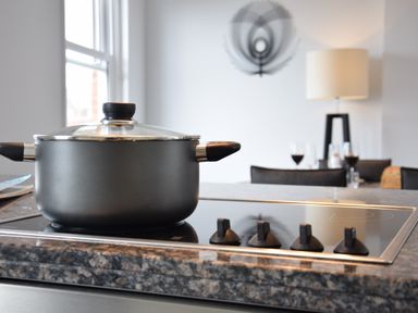 A kitchen with a black cooking pot on a stovetop and a dining area with chairs glasses and a lamp at Pier View Southwold