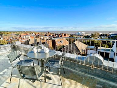 A rooftop terrace with a round table and four chairs overlooking houses and the sea at Pier View Southwold